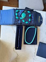 All three jewelry items in Stauer presentation cases: green pendant necklace, bracelet, turquoise bead necklace