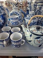Front grouping showing teapot with bamboo handle, four cups, stacked saucers and additional blue-white ware