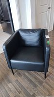 Front view of black faux leather armchair showing seat cushion and metal legs
