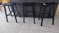 Three black wood counter-height stools front view against counter