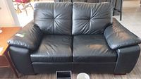 Front view of black leather-look loveseat showing overall design and condition