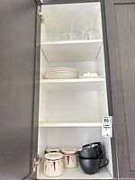 Cabinet view showing wine glasses, plates, butter dish, and mugs