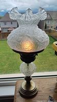 Full view of lit frosted glass hurricane table lamp on window sill