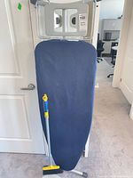Front view of ironing board with broom and dustpan leaning against it