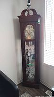 Full view of grandfather clock curio cabinet showing clock face, glass door and shelves