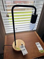 Full view of lamp on wooden table showing metal arm, wood base, power cord