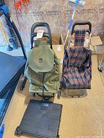Two rolling shopping carts side by side with green bag cart in front of folded plastic base and plaid bag cart on metal frame