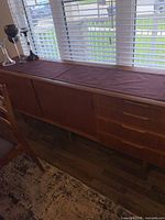 Full view of teak credenza under window showing drawers and sliding doors