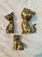 Front view of three brass cat figurines showing design details and patina
