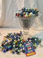 Glass pedestal compote filled with multicolor marbles; additional marbles and promotional tag in foreground