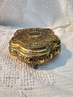 Closed ornate gilt metal jewelry box showing exterior detailing and feet
