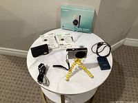 All items arranged on table: camera on tripod, box, manuals, charger, cables, pouch