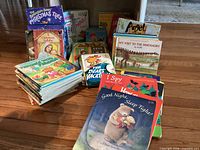 Three stacks of assorted children’s books spread on wood floor showing covers and sizes