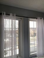 Two windows dressed with white sheer panels on black rod