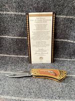 Knife open displaying stainless blade and handle details beside certificate