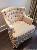 Front view of beige polka dot tufted accent armchair with skirted base and removable cushion