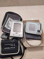 Two BIOS blood pressure monitors with cuffs, adapter and case displayed