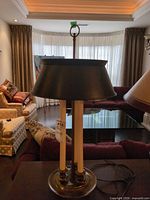 Front view of brass/bronze metal table lamp with black shade on table showing three candle-style columns and power cord