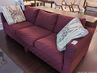front angled view of burgundy 3-seater sofa with two patterned pillows