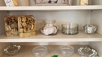 Shelf view showing stone bookends, glass vases with seashells, cylindrical vase, crystal dishes on lower shelf