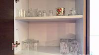 Cabinet view showing multiple clear tumblers, shot glasses and butter dish