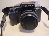 Front view of Pentax SF1 camera with lens, cap, strap, box partially visible