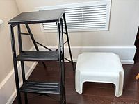 Black metal folding ladder beside white plastic stool