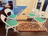 Four white metal folding chairs with green vinyl seats around boxed Meco folding table