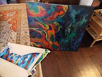 Two stretched canvases with abstract multicolour designs and rolled canvases beside them