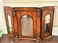 Front view showing mirrored doors, floral inlay, carved appliques, overall form