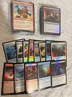 Stack of sleeved foil MTG cards with visible front card Talaji Clancaller plus loose spread of other foils