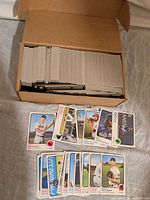 Open cardboard box filled with stacked baseball cards and spread of selected cards in front