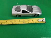 Left side view of silver 1997 Corvette model beside tape measure showing length ~12 cm