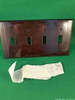 Front view of brown four-gang switch plate with screws on green background