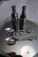 Overall view of four items: two bottle-form shakers and two souvenir spoons