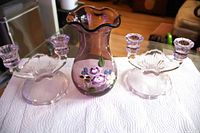 Three lilac glass pieces on white cloth: pair of candle holders and vase