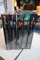 All five sealed Supernatural DVD box sets standing side-by-side showing spines