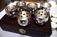 Six silverplate star-cutout tealight holders displayed on wooden case