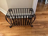 Front view of black wrought iron log holder showing overall shape and scroll feet