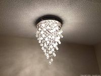 Chandelier lit, showing chrome canopy and cascading clear crystal drops