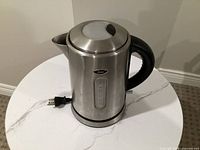 Front view of stainless steel Oster electric kettle showing water gauge, power cord, and logo