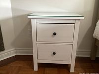 Front view of nightstand showing two drawers, glass top, black knobs