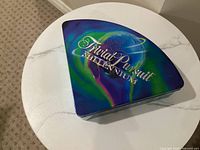 Closed pie-shaped metal tin showing Trivial Pursuit Millennium logo