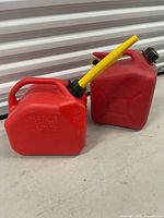 Two red 10 L gasoline cans on floor, one with spout attached