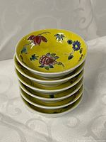 Stack of six yellow porcelain sauce dishes with famille rose floral pattern