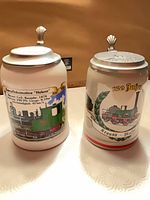 Front view of both ceramic beer steins showing train graphics and pewter lids
