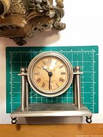 Silver metal column clock on mat for scale