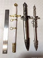 Three daggers in scabbards beside 12 in. ruler