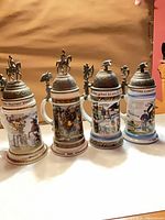 Front view of all four steins showing decorations and lids