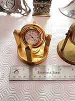 Brass gimbal-style desk clock foreground; triangular pewter and column pewter clocks visible behind